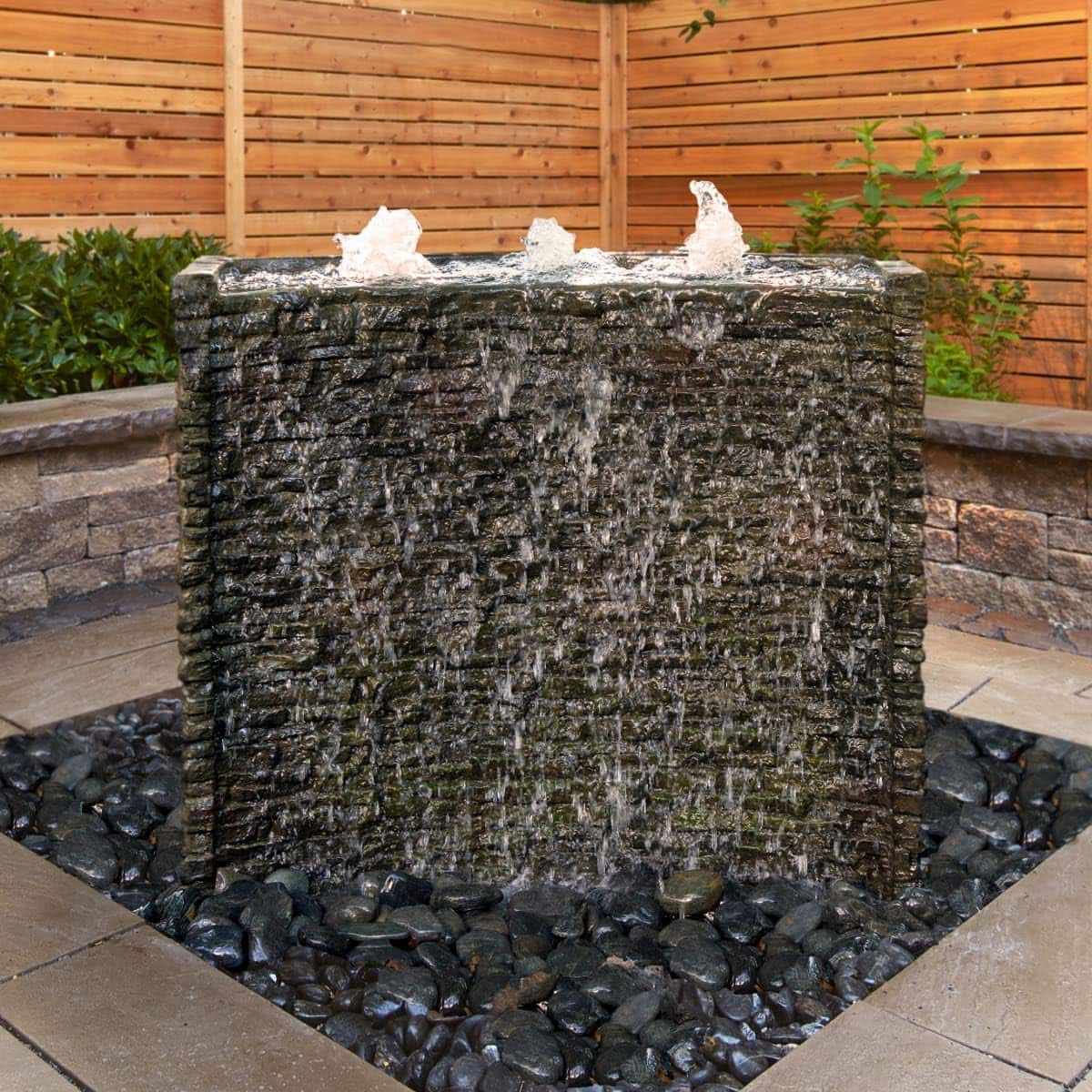 Water flows over a square stone fountain outdoors. - Stacked Slate Wall Fountain Kit – 32″ H (81 cm)