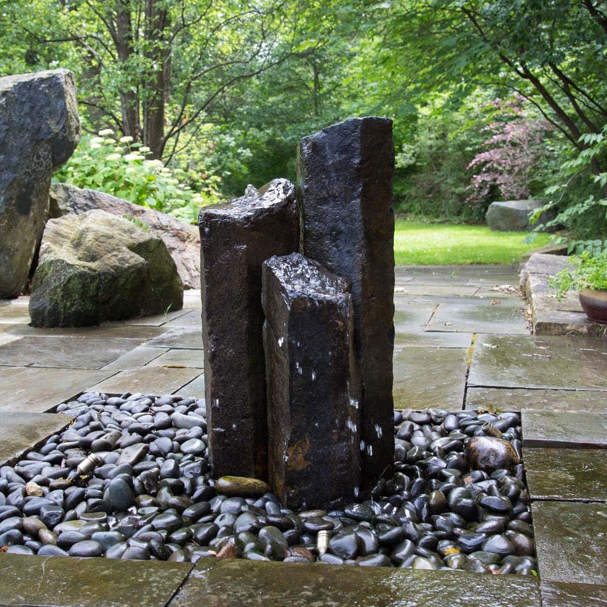 Rock fountain in a garden with greenery. - Natural Mongolian Basalt Columns Set Of 3 Fountain Kit