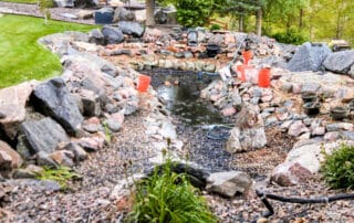 Rocky garden pond under construction with orange buckets.