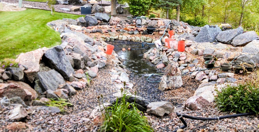 Rocky garden pond under construction with orange buckets.
