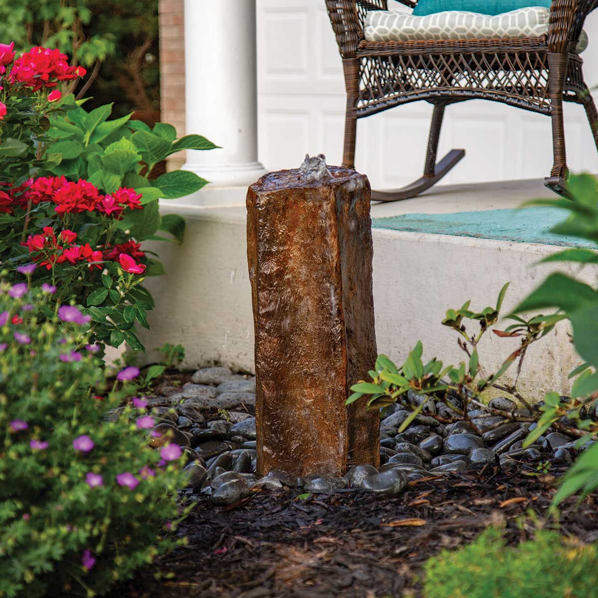 Rustic garden fountain with flowers and chair.
