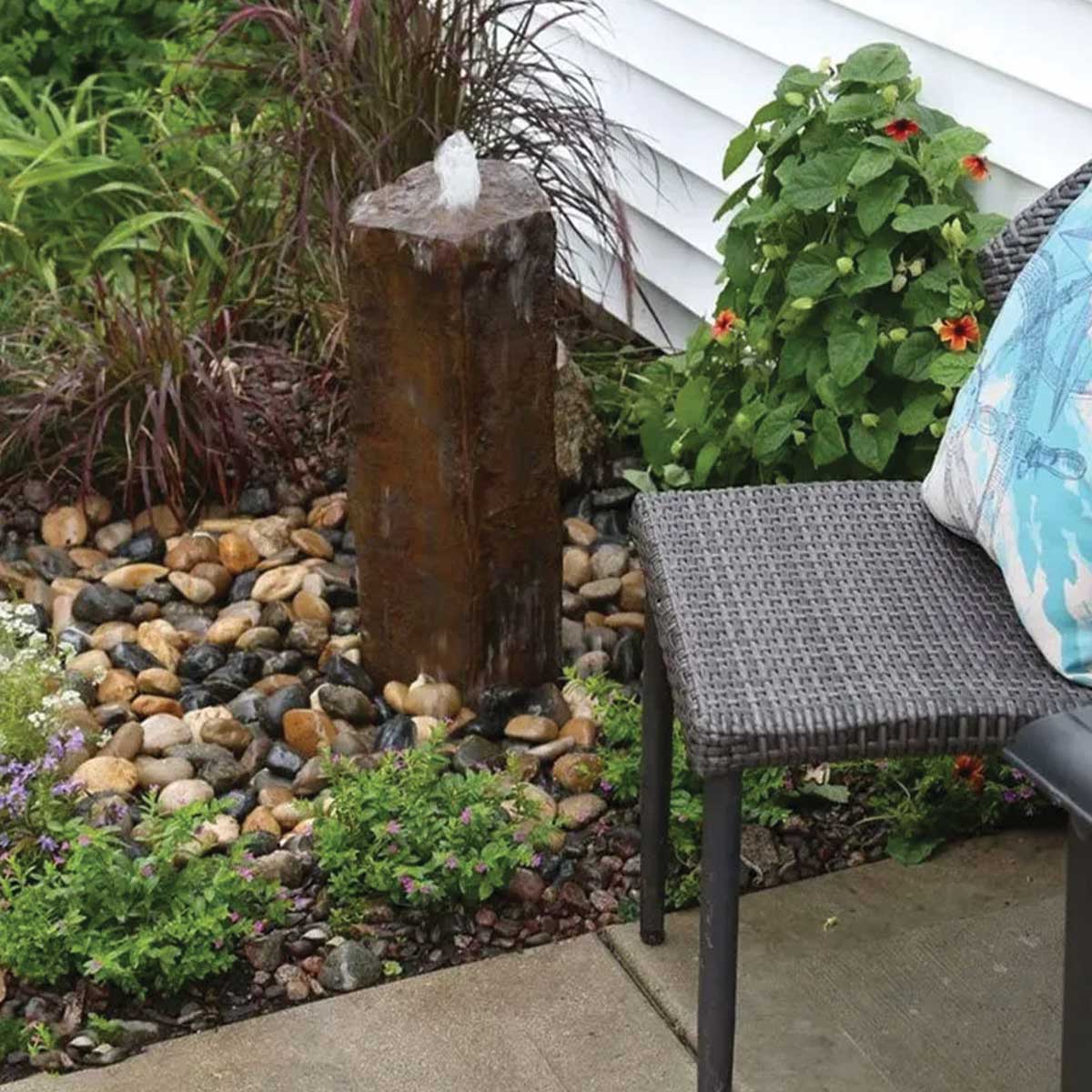 Garden fountain with stones and plants near chair.