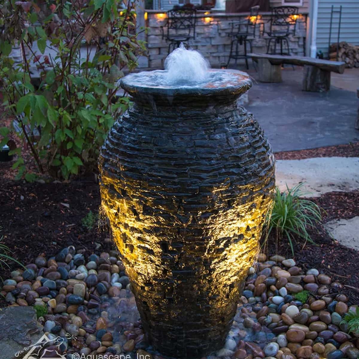Illuminated water feature vase in garden setting. - Stacked Slate Urn Fountain Kit – 45″ H (114 cm)